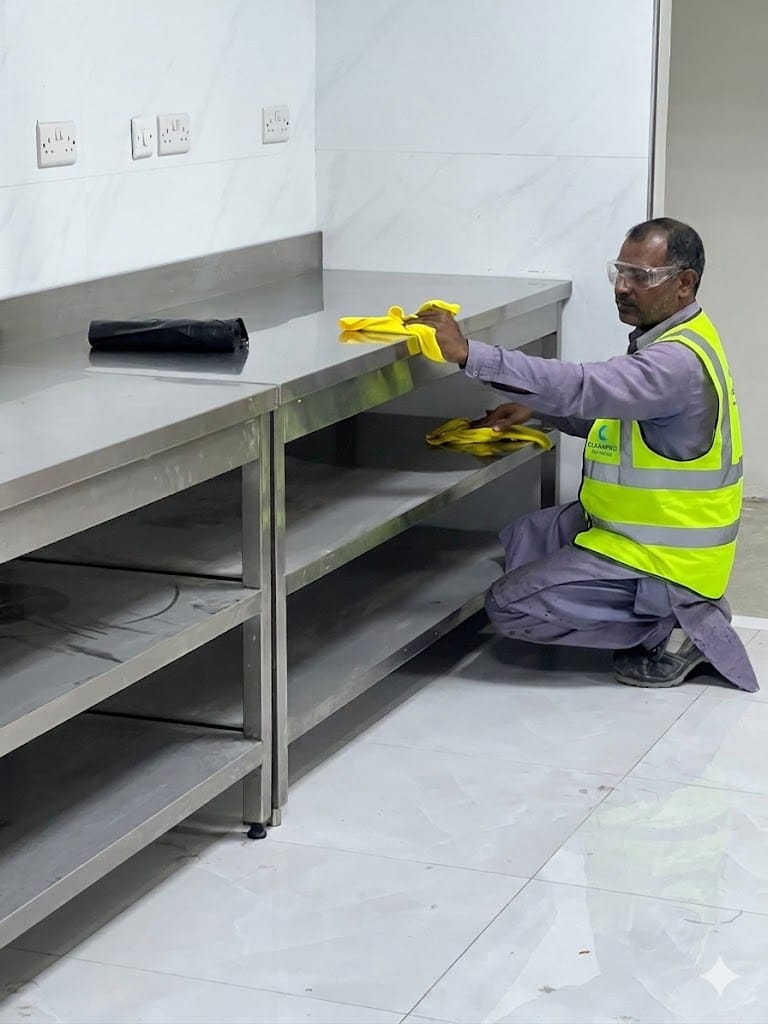 Compass FM cleaning operative sanitising stainless steel work surfaces in a commercial kitchen facility.